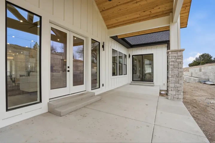 Covered patio with a wood-finish ceiling, board-and-batten siding, and stone-clad column