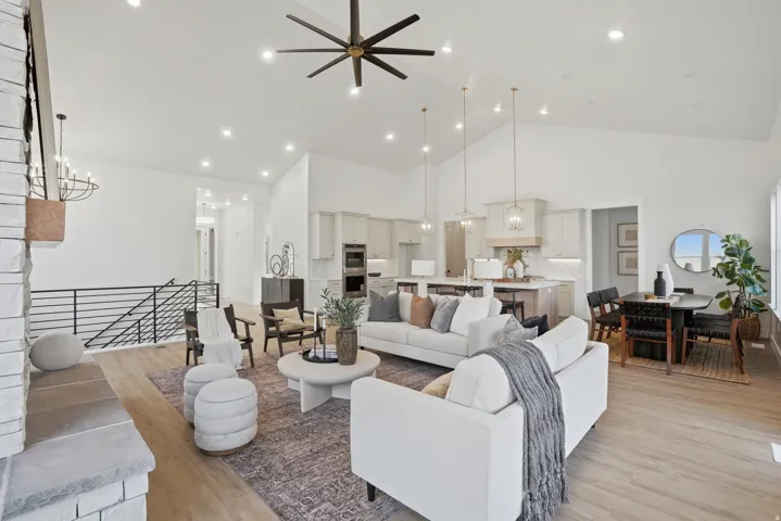 Vaulted ceiling with recessed lighting and a ceiling fan, a stone fireplace, wood-finish flooring, and a modern kitchen with a large island and pendant lighting