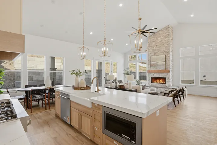 Spacious open-concept interior featuring vaulted ceilings, wood-finish flooring, a kitchen island with stone countertops, and a stone fireplace