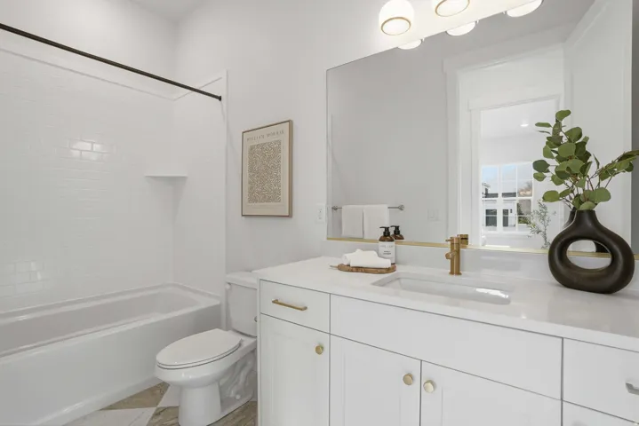 White subway tile tub surround, built-in shelving, white floating vanity with integrated sink, brass-finish faucet, and modern vanity lighting