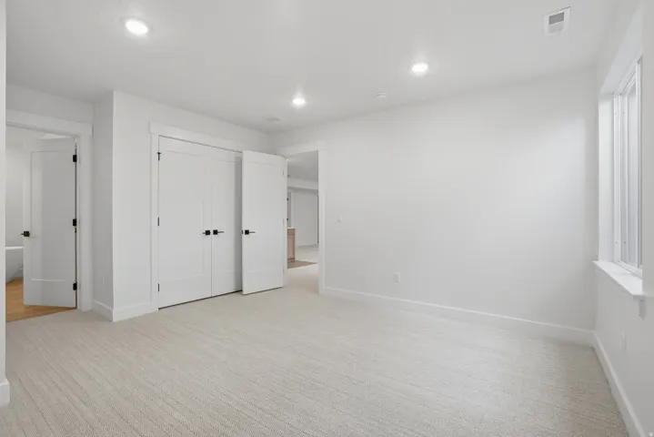 Recessed lighting, light-toned carpet flooring, a window with natural illumination, and white interior doors with black hardware