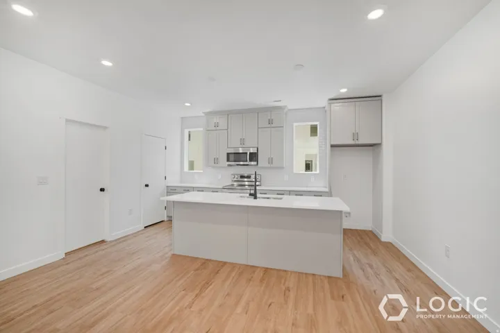 Modern kitchen featuring light gray cabinetry, stainless steel appliances, a white subway tile backsplash, and an island with a white countertop