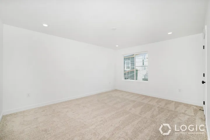 Neutral carpet flooring, white painted walls, recessed lighting, and a single window with white trim