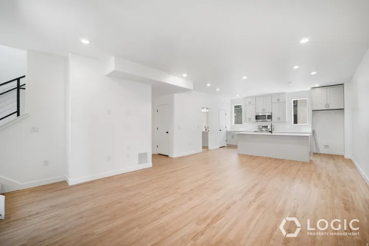 Open-concept living area featuring wood-finish flooring, recessed lighting, and a modern kitchen with light gray cabinetry and stainless steel appliances
