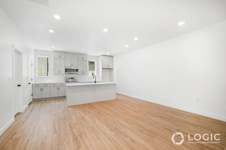 Open-concept kitchen and living area featuring wood-finish flooring, recessed lighting, and a kitchen island with a black faucet