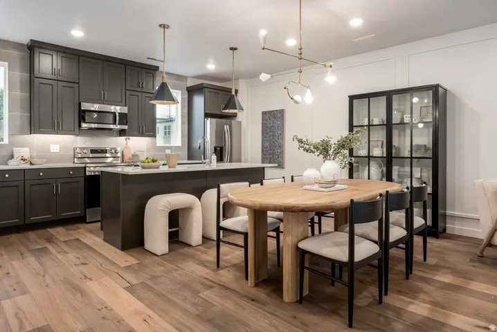 Open-concept kitchen and dining area featuring wood-finish flooring, dark shaker-style cabinetry, stainless steel appliances, and a central island with countertop seating