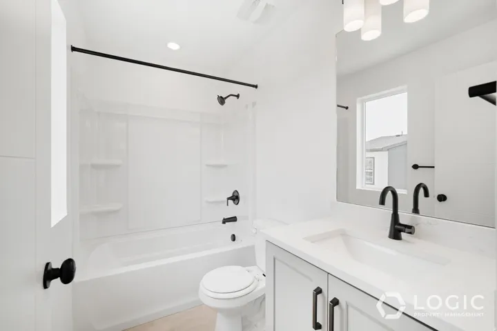 White bathroom featuring a built-in tub with shower, single vanity with integrated sink, and matte black fixtures