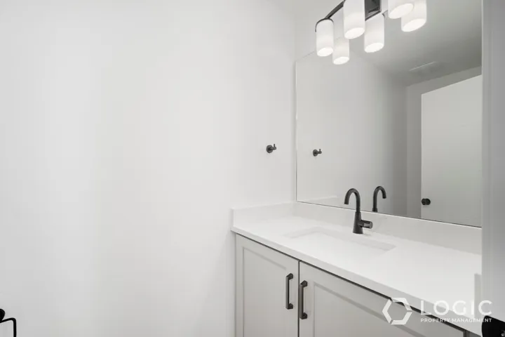 White countertop with integrated sink, black matte faucet, light gray cabinetry, black hardware, and an oversized mirror