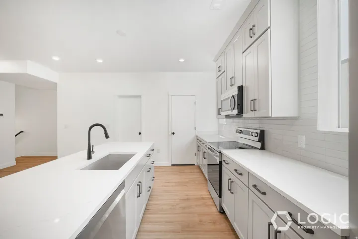Kitchen featuring a large island with an undermount sink and matte black faucet, light wood-finish flooring, white shaker-style cabinetry, and stainless steel appliances