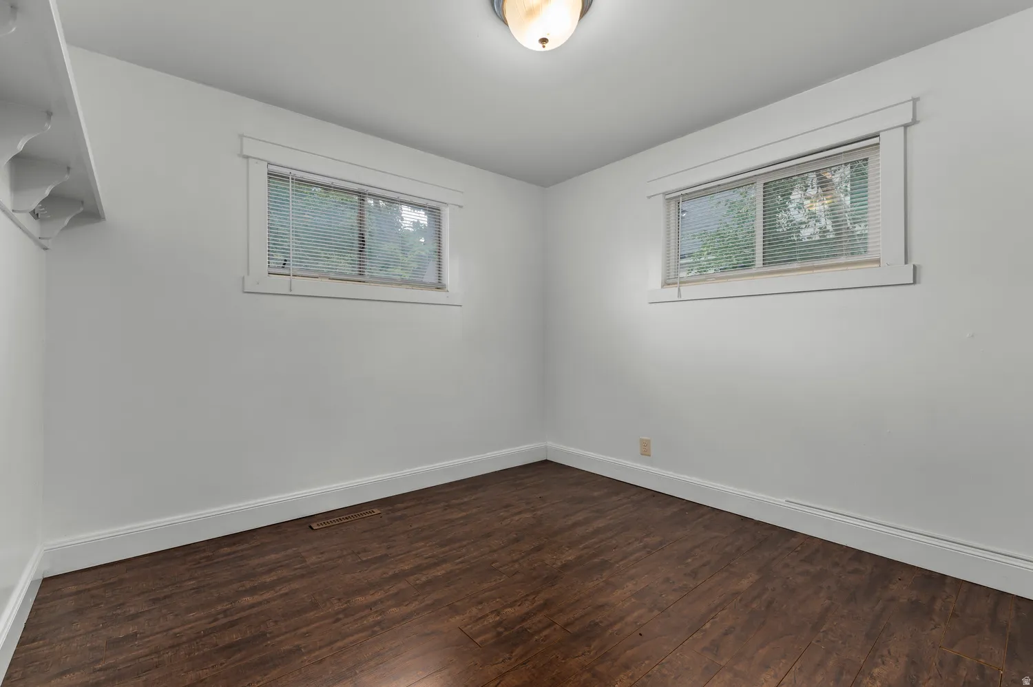 White walls, wood-finish flooring, two windows with blinds, and ceiling-mounted light fixture
