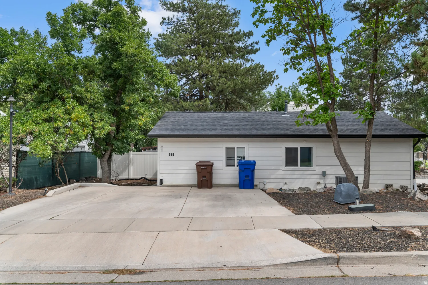 Unit #2White siding exterior with a dark shingled roof, featuring mature trees and a concrete driveway