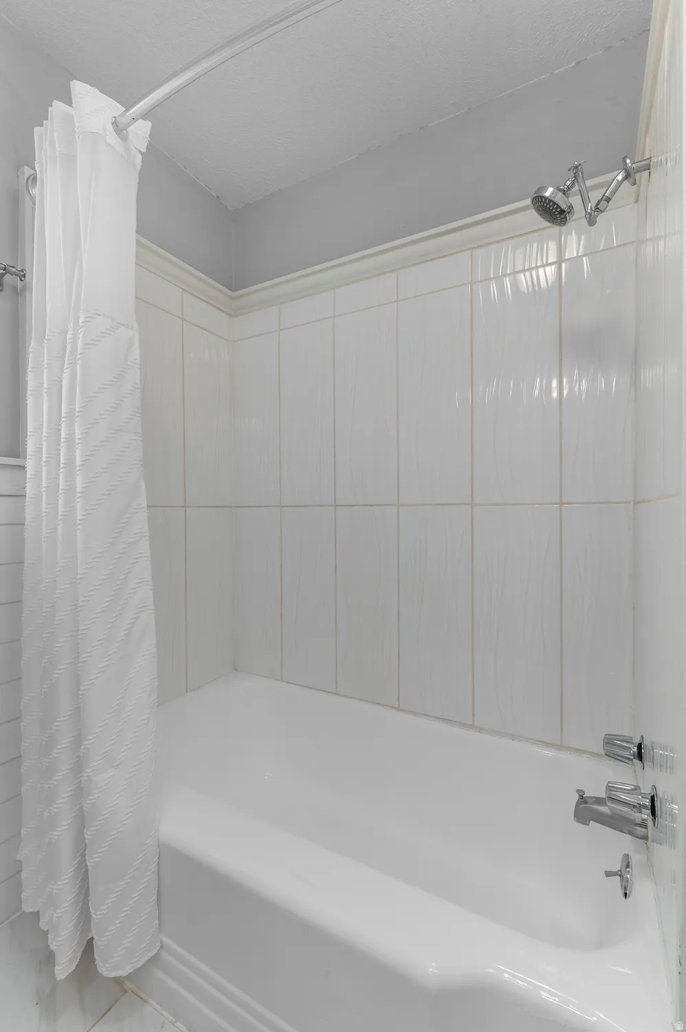 White bathtub with chrome fixtures and white tiled surround