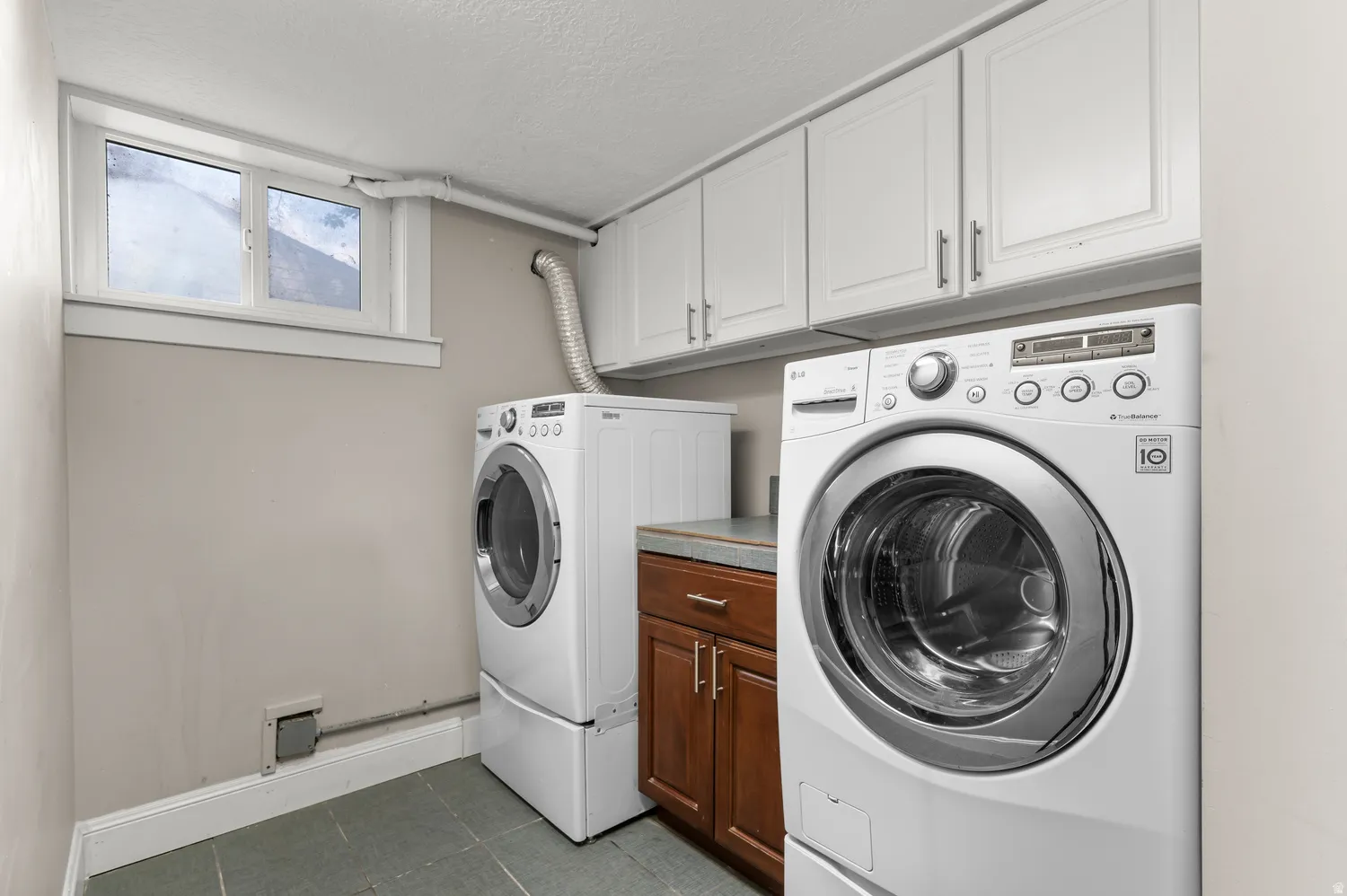 Laundry area featuring white upper cabinetry, a wood-finish base cabinet, a counter surface, and tile flooring