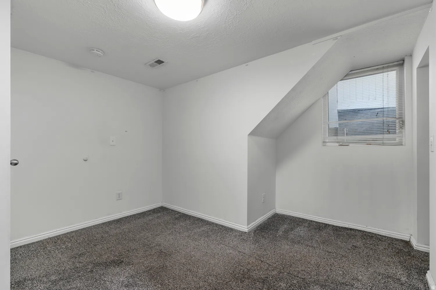 Carpeted flooring with white baseboards, a single window with blinds, and a flush mount ceiling light fixture