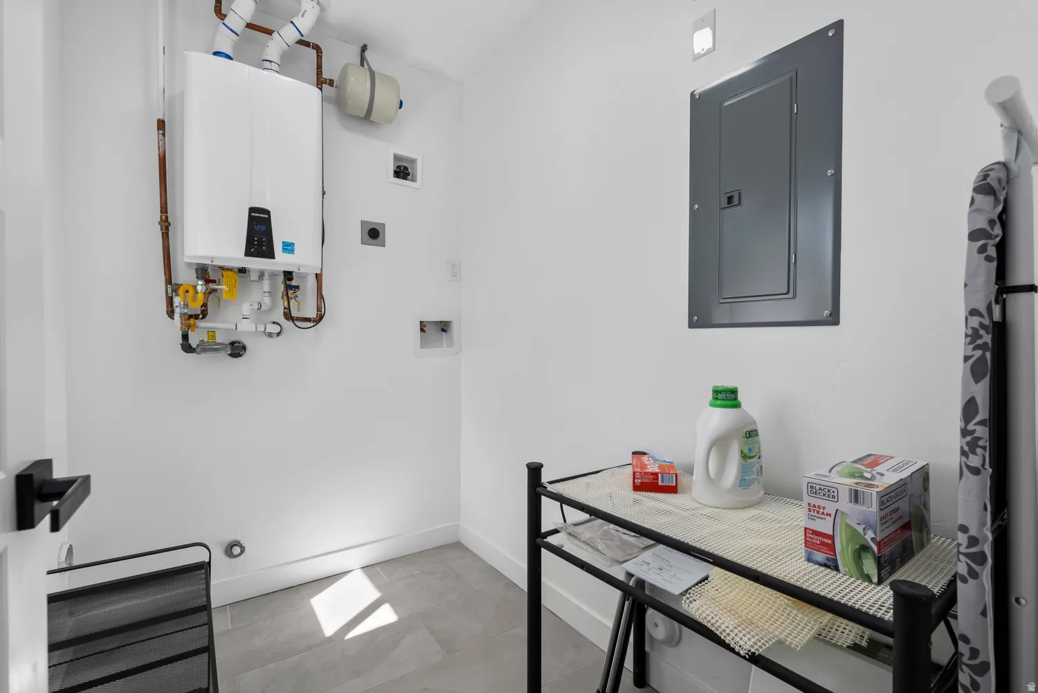 Unit #2Wall-mounted tankless water heater with copper piping, electrical panel, and gray tile flooring