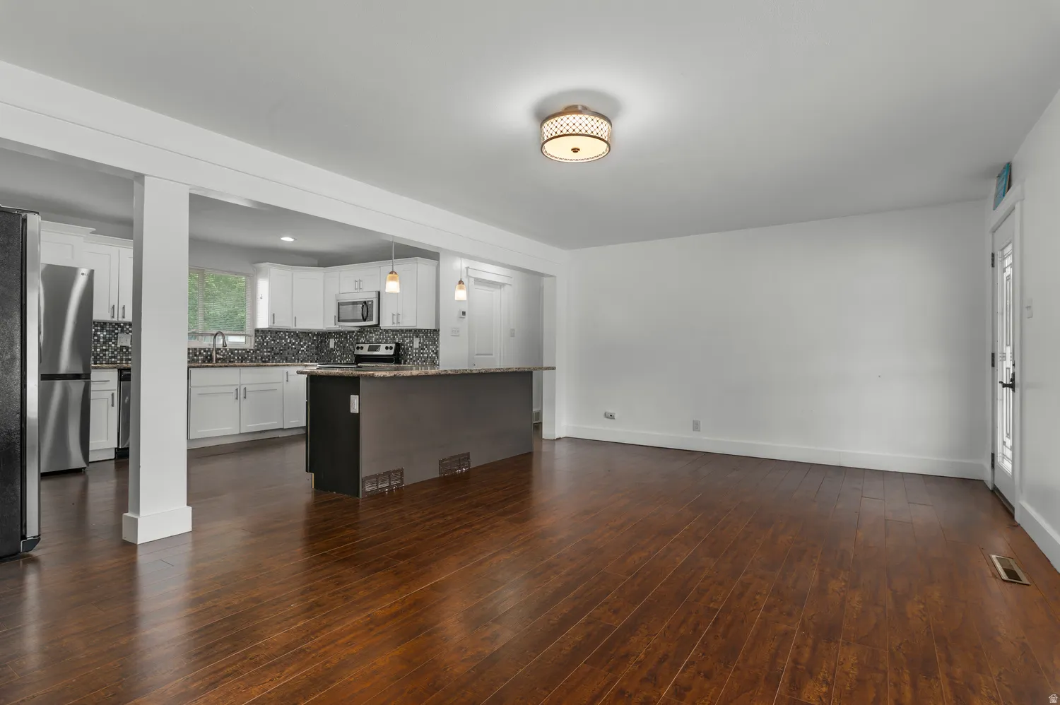 Rich wood-finish flooring throughout, white painted walls, and a contemporary ceiling light fixture