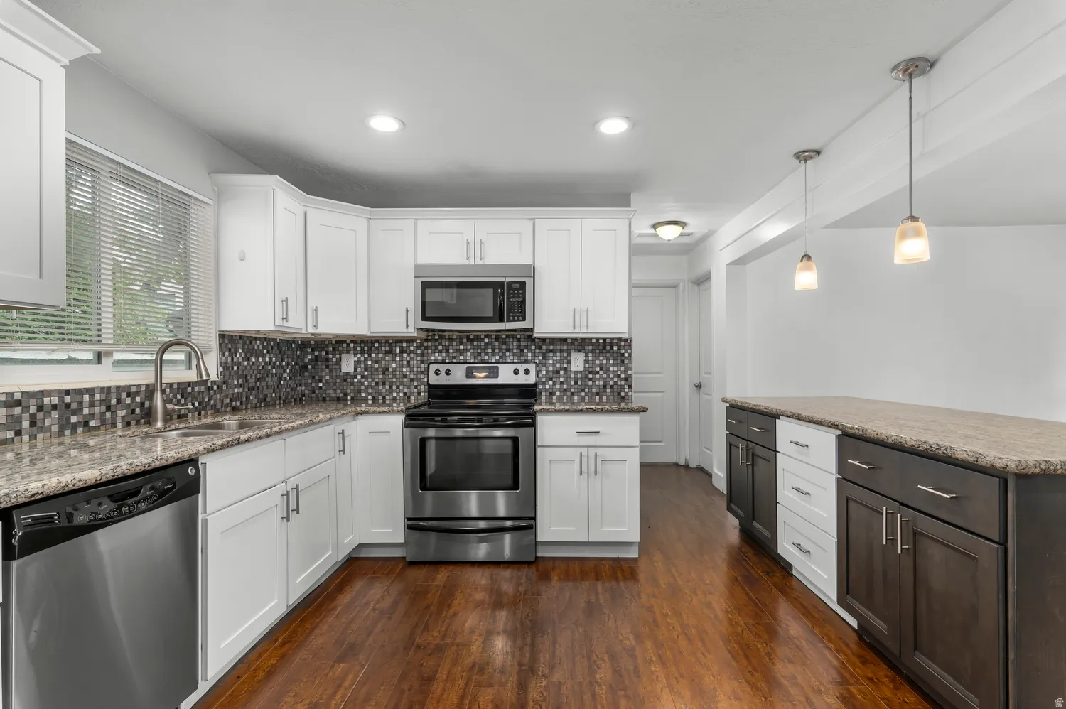 Kitchen featuring stainless steel appliances, wood-finish flooring, white cabinetry, a tiled backsplash, and stone countertops