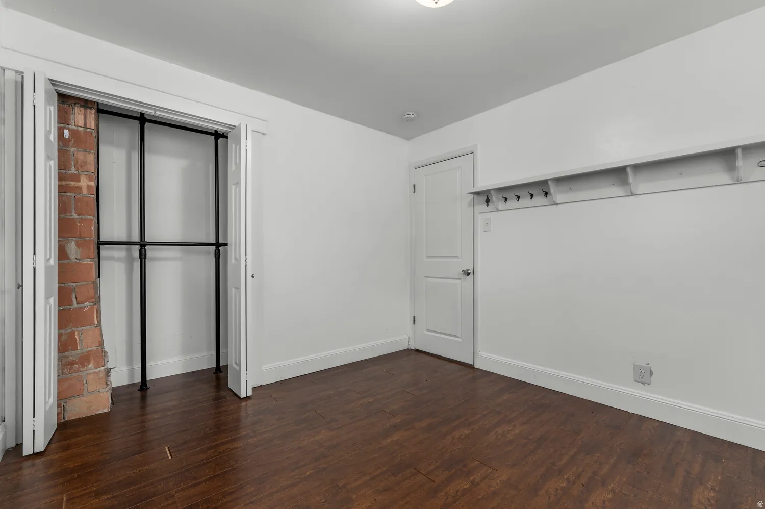 Wood-finish flooring, exposed brick detail, bi-fold closet doors, built-in shelving, and a paneled door