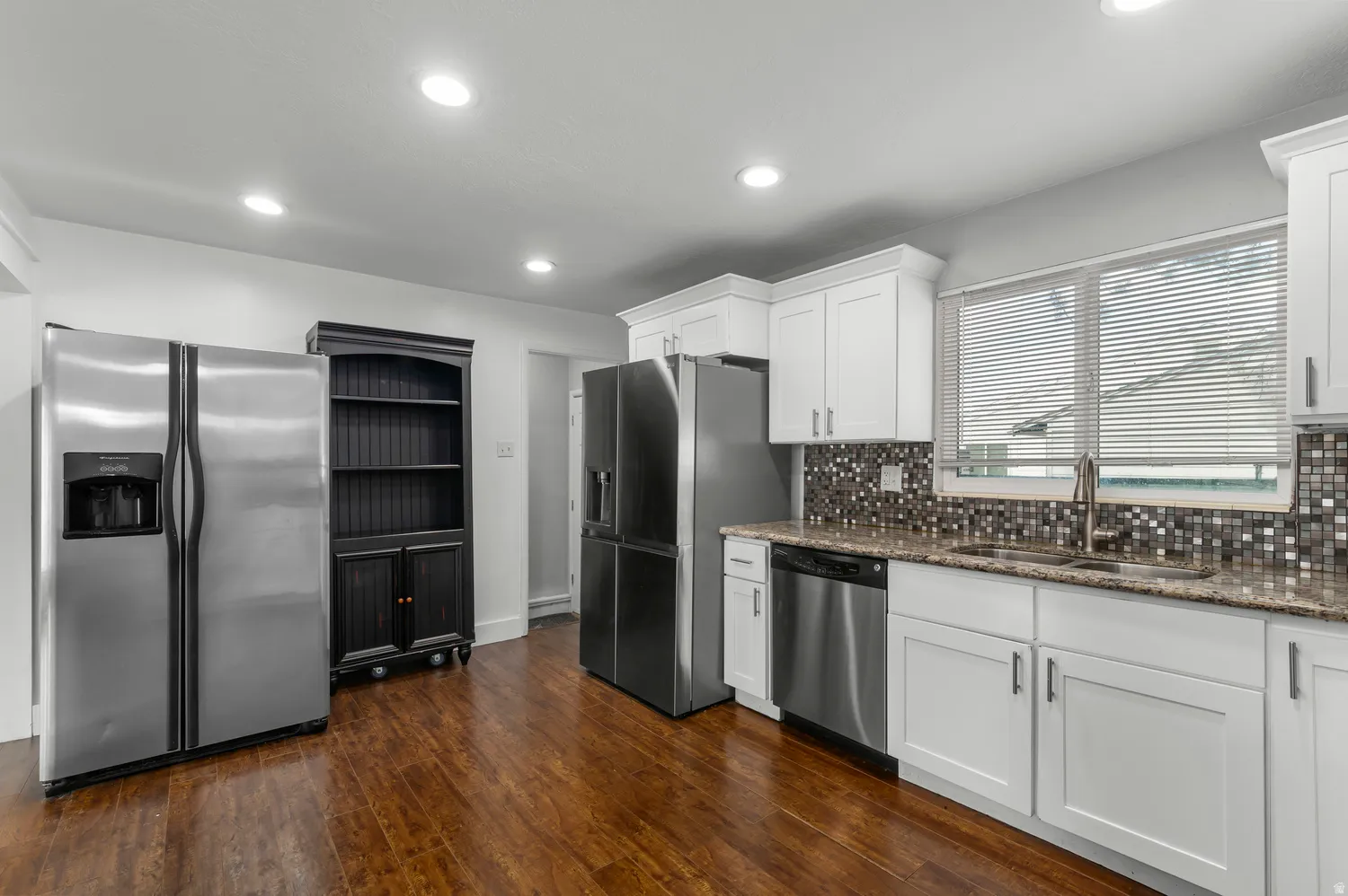 White cabinetry, granite-style countertops, stainless steel appliances, mosaic tile backsplash, and wood-finish flooring