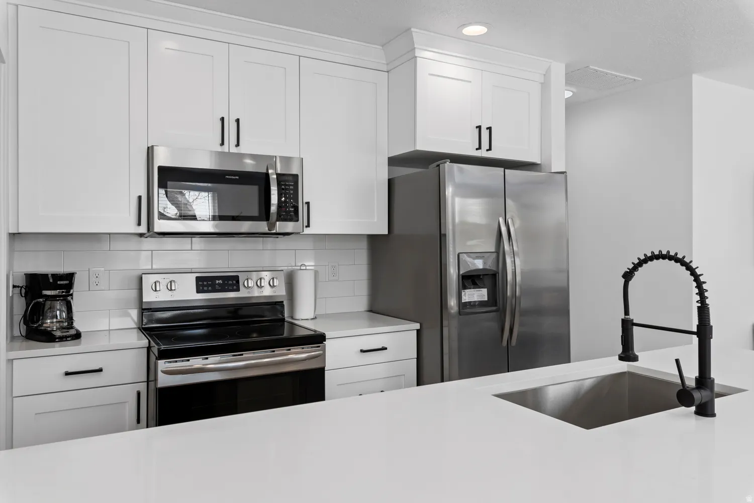 Unit #2White shaker-style cabinetry with matte black hardware, stainless steel appliances, subway tile backsplash, and a large kitchen island with an undermount sink
