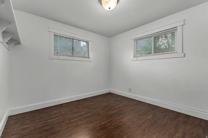 White walls, wood-finish flooring, two windows with blinds, and ceiling-mounted light fixture