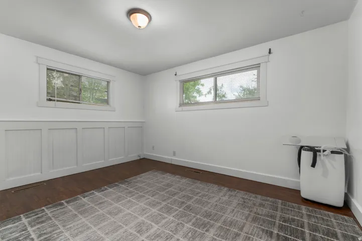 Dark wood-finish flooring, white board and batten wall accent, two distinct windows, and a flush-mount ceiling light fixture