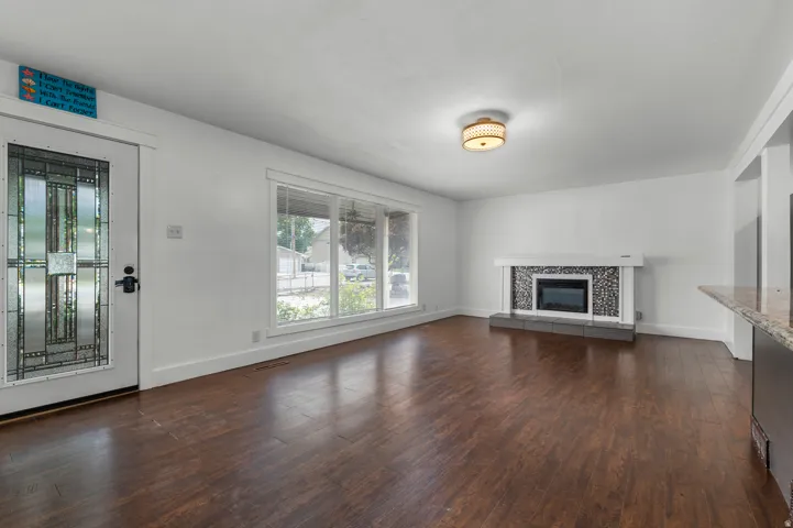 Dark wood-finish flooring, white walls, and a recessed electric fireplace with a decorative tile surround