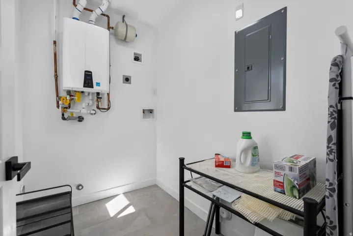 Unit #2Wall-mounted tankless water heater with copper piping, electrical panel, and gray tile flooring