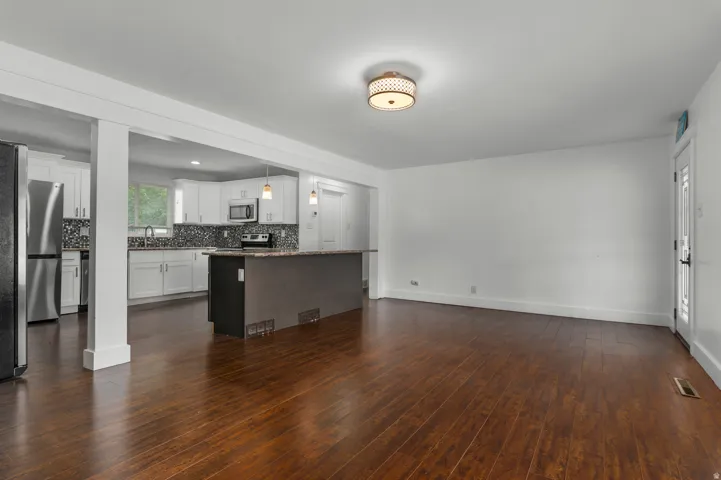 Rich wood-finish flooring throughout, white painted walls, and a contemporary ceiling light fixture