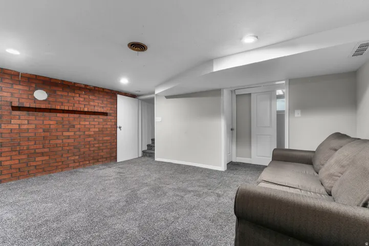 Spacious room featuring a brick accent wall, recessed lighting, and soft gray carpeting