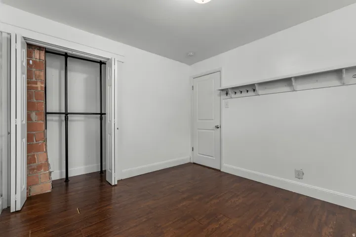 Wood-finish flooring, exposed brick detail, bi-fold closet doors, built-in shelving, and a paneled door