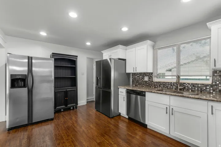 White cabinetry, granite-style countertops, stainless steel appliances, mosaic tile backsplash, and wood-finish flooring