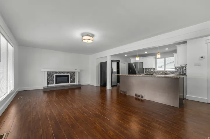 Wood-finish flooring throughout, a modern fireplace with a tiled surround, a kitchen island with pendant lighting, white cabinetry, and stainless steel appliances