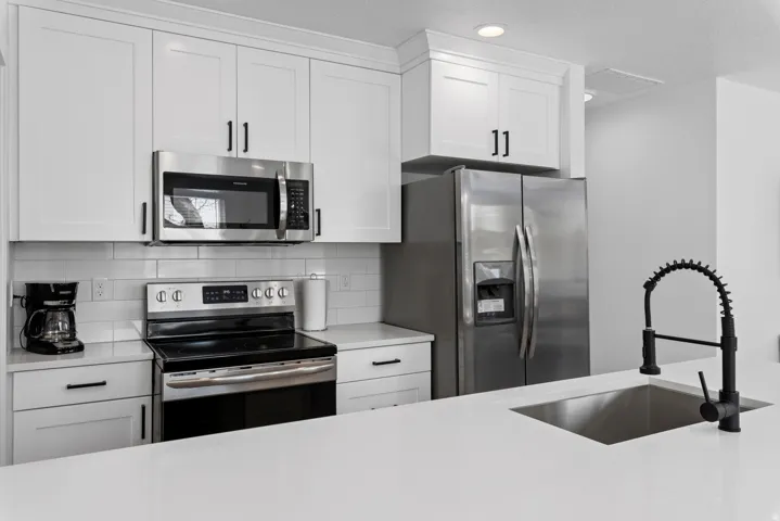 Unit #2White shaker-style cabinetry with matte black hardware, stainless steel appliances, subway tile backsplash, and a large kitchen island with an undermount sink