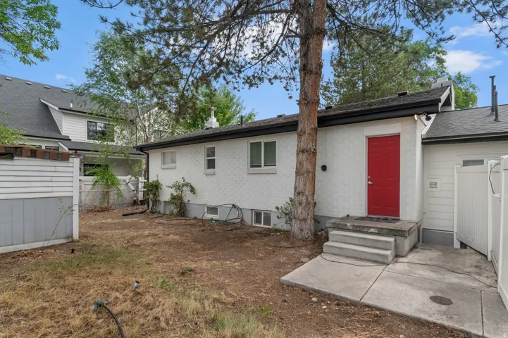 White exterior with a vibrant red entry door, concrete steps, and a concrete patio area