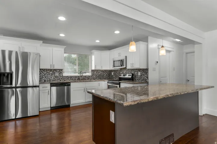 Kitchen featuring white cabinetry, stainless steel appliances, mosaic tile backsplash, and a large island with a stone countertop