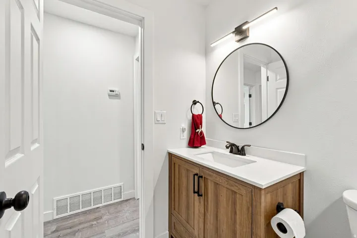 Wood-finish vanity with a white countertop and integrated sink, matte black faucet, and a round black-framed mirror