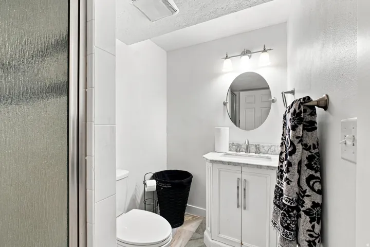White vanity with a stone countertop, an oval mirror, and a three-light fixture