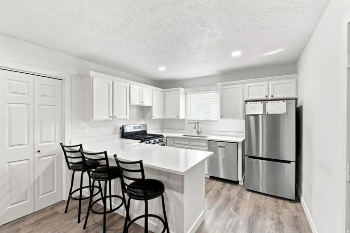 White cabinetry with crown molding, stainless steel appliances, wood-finish flooring, white countertop surfaces, and an integrated kitchen island