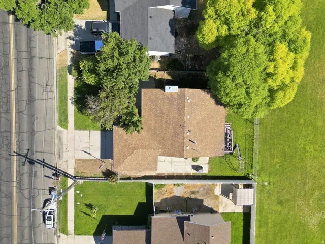 Brown shingle roof, paved driveway, concrete walkway, and a landscaped front lawn