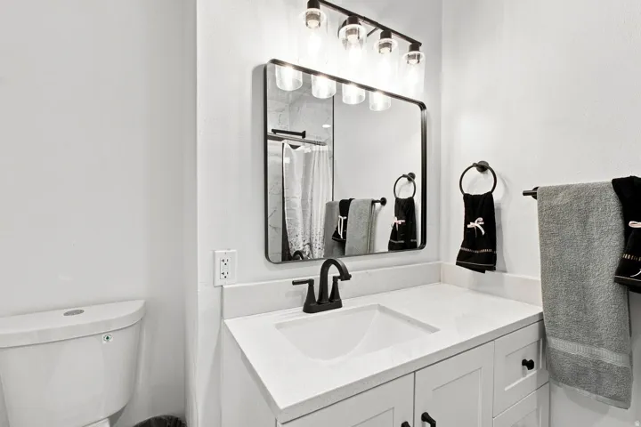 Contemporary bathroom featuring a white vanity with an integrated sink, a dark bronze faucet, and a coordinating framed mirror