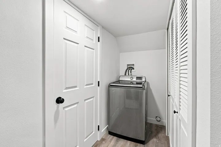 Interior laundry area featuring wood-finish flooring and a white louvered bifold door