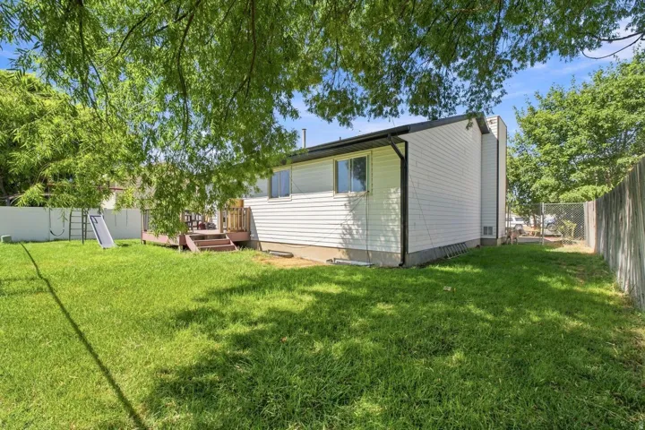 Expansive backyard featuring a manicured lawn, a multi-level wood deck, a white privacy fence, and mature trees