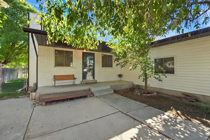 White brick exterior with dark trim accents, concrete patio, and a mature tree providing shade