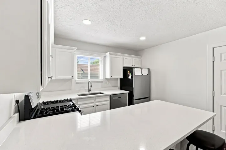 Kitchen featuring white cabinetry, light countertops, stainless steel appliances, and a gas range