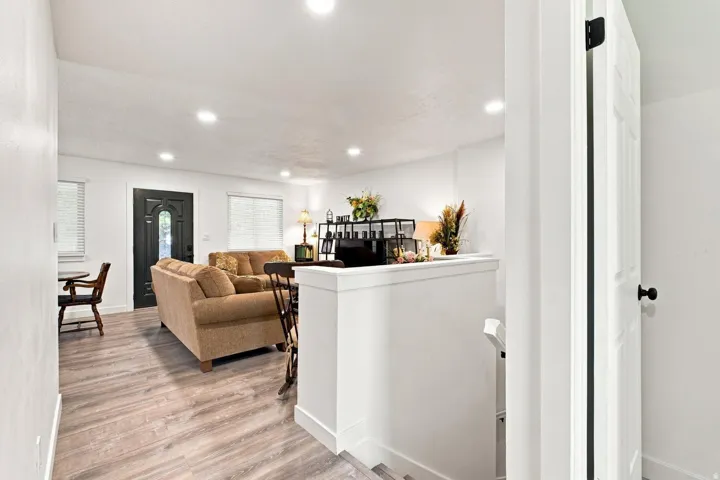 Recessed lighting, wood-finish flooring, white walls, black paneled door, and white trim