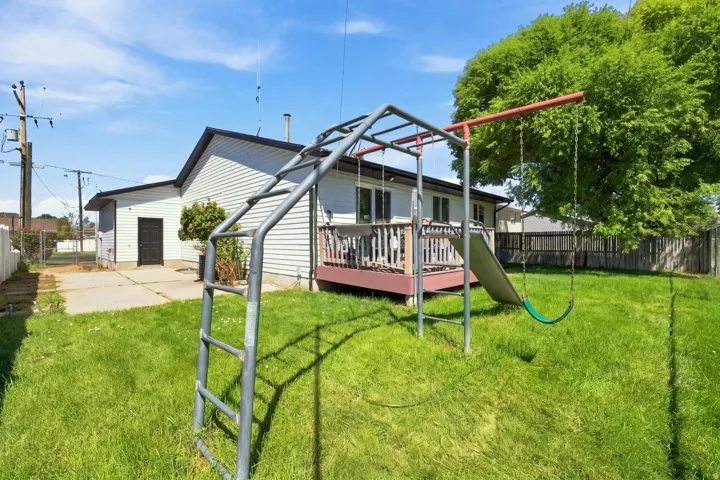 Expansive backyard featuring a manicured lawn, concrete patio, and a wood-finish deck with railings