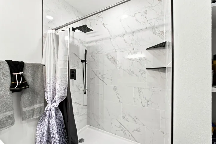 Shower with marble-patterned tile, matte black fixtures, a glass enclosure, and built-in shelving
