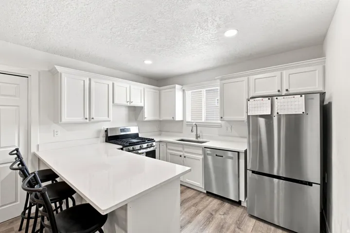 Modern kitchen featuring white shaker cabinets, white countertops, stainless steel appliances, and wood-finish flooring