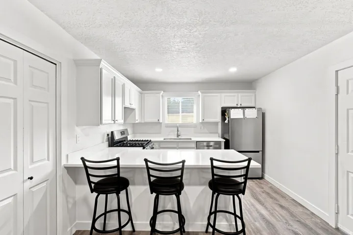 Kitchen featuring white cabinetry, light-toned countertops, wood-finish flooring, stainless steel appliances, and a breakfast bar